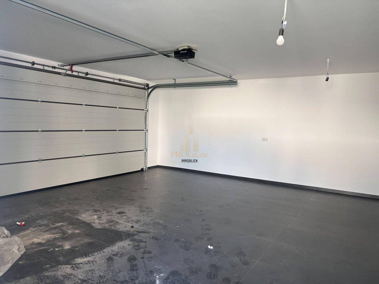 Geräumige Garage mit Fliesenboden und automatischem Garagentor.