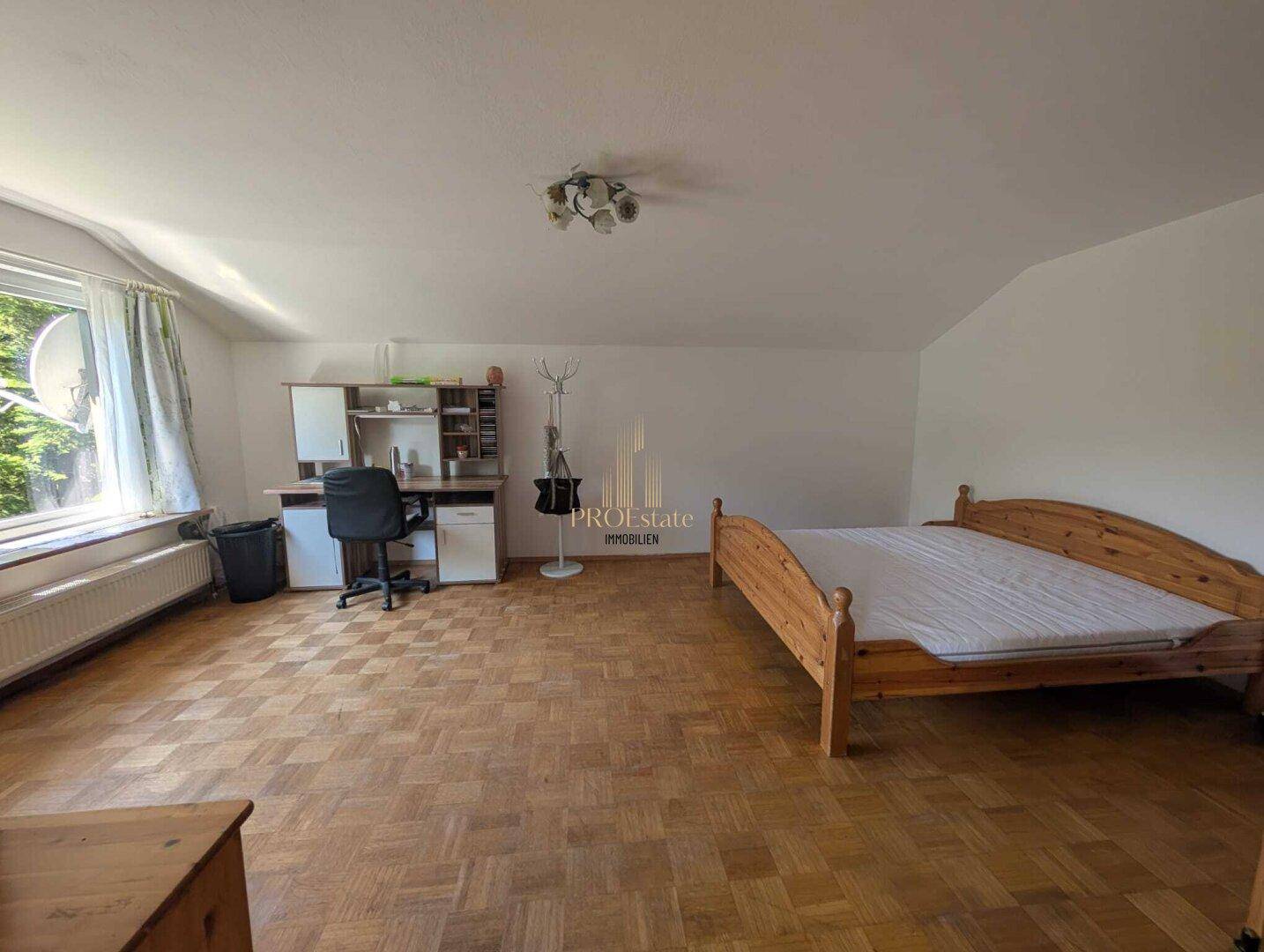 Geräumiges Schlafzimmer mit Parkettboden, Holzmöbeln und einem Arbeitsbereich am Fenster.
