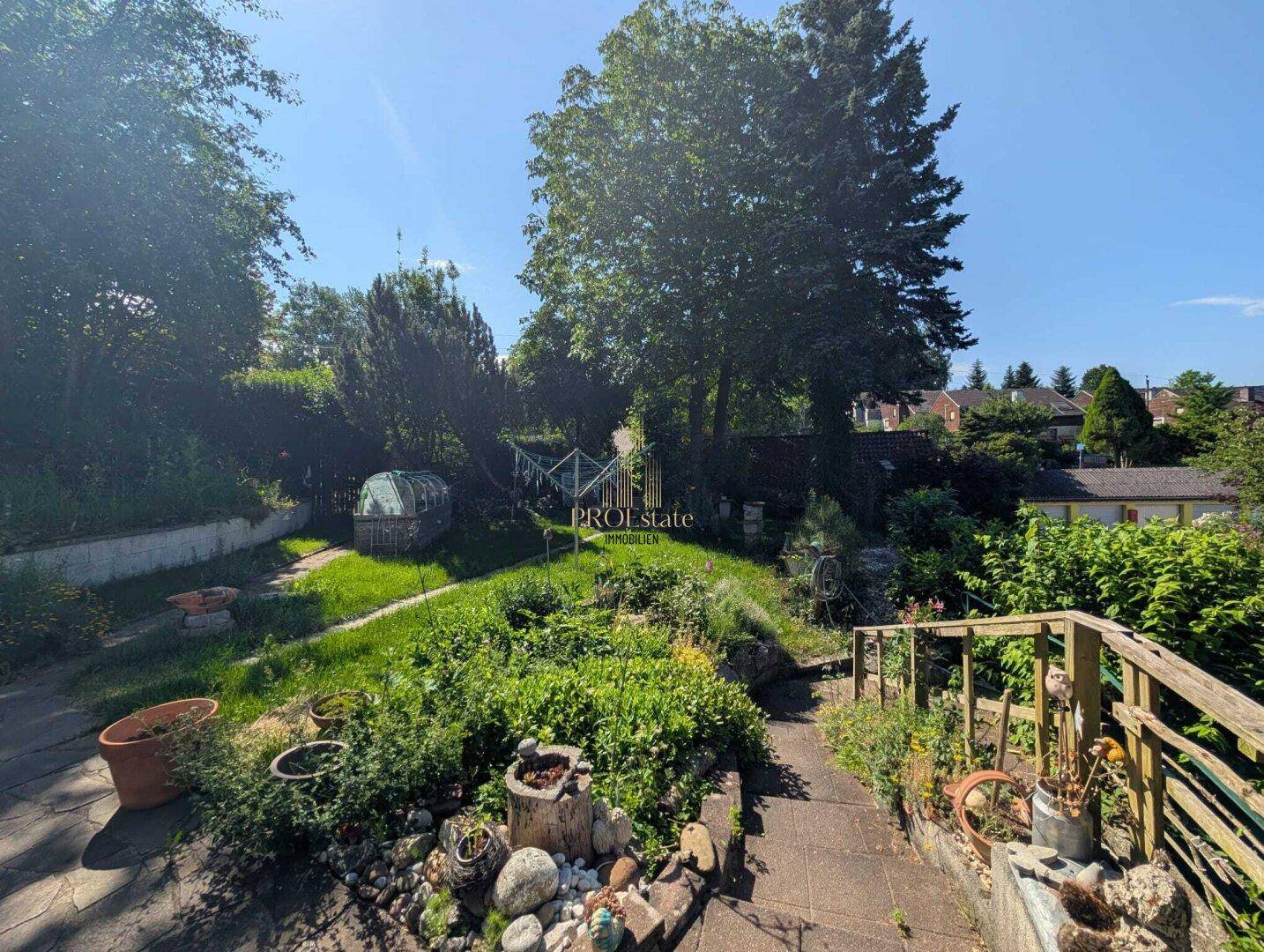 Gepflegter Gartenbereich mit einem Weg, verschiedenen Pflanzen und altem Baumbestand.