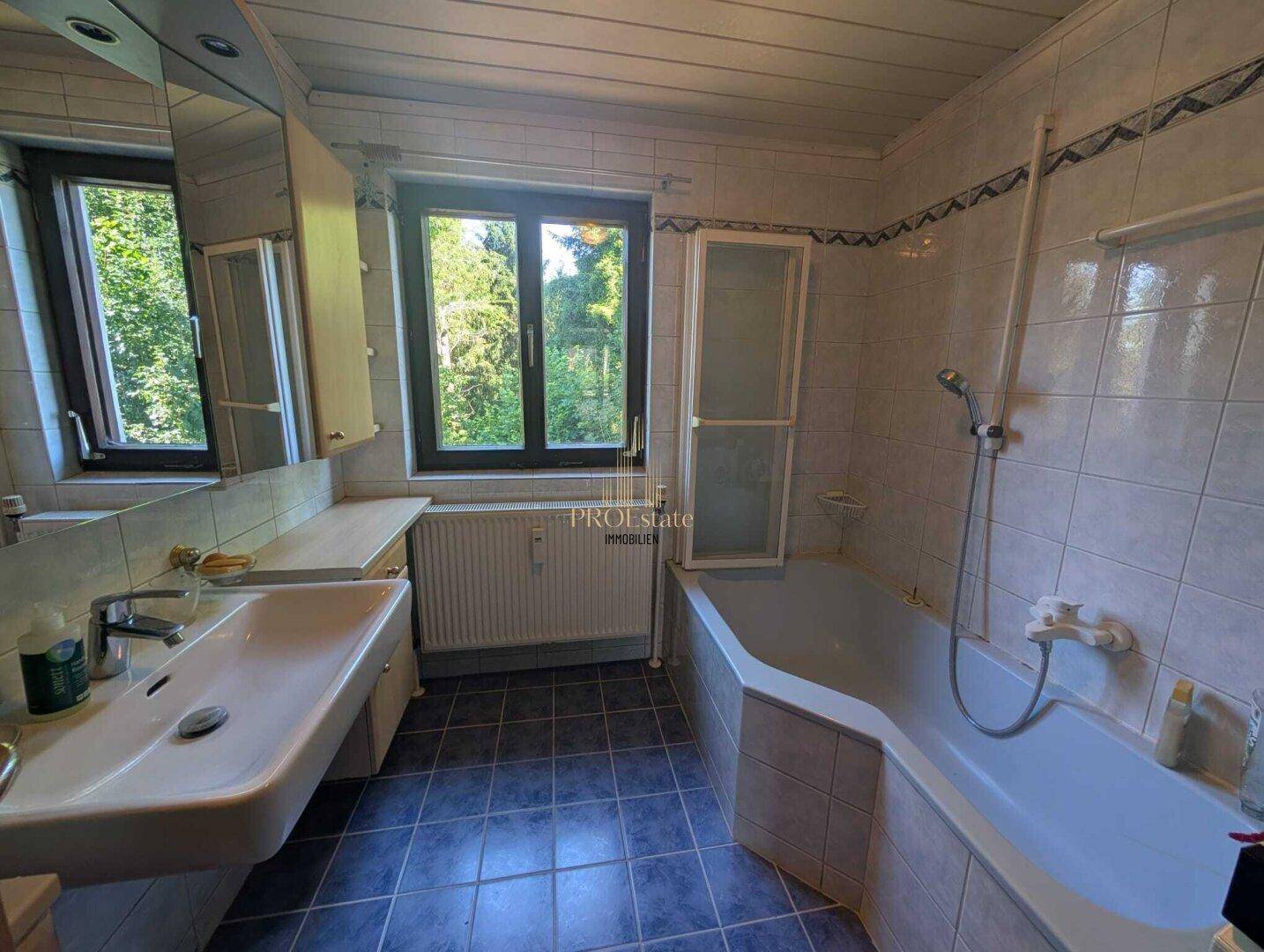 Badezimmer mit Badewanne, Waschbecken, blauen Fliesen und einem Fenster.