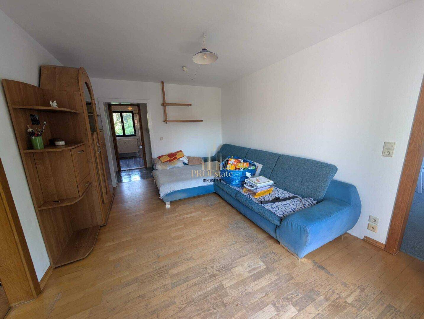 Wohnraum mit blauem Sofa, Holzmöbeln und hellem Laminatboden.