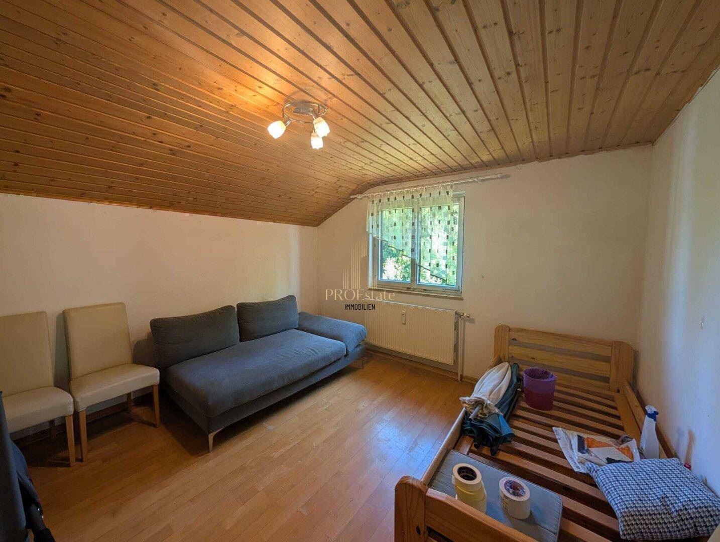Helles Zimmer mit Holzdecke, Holzboden und einem Schlafsofa.