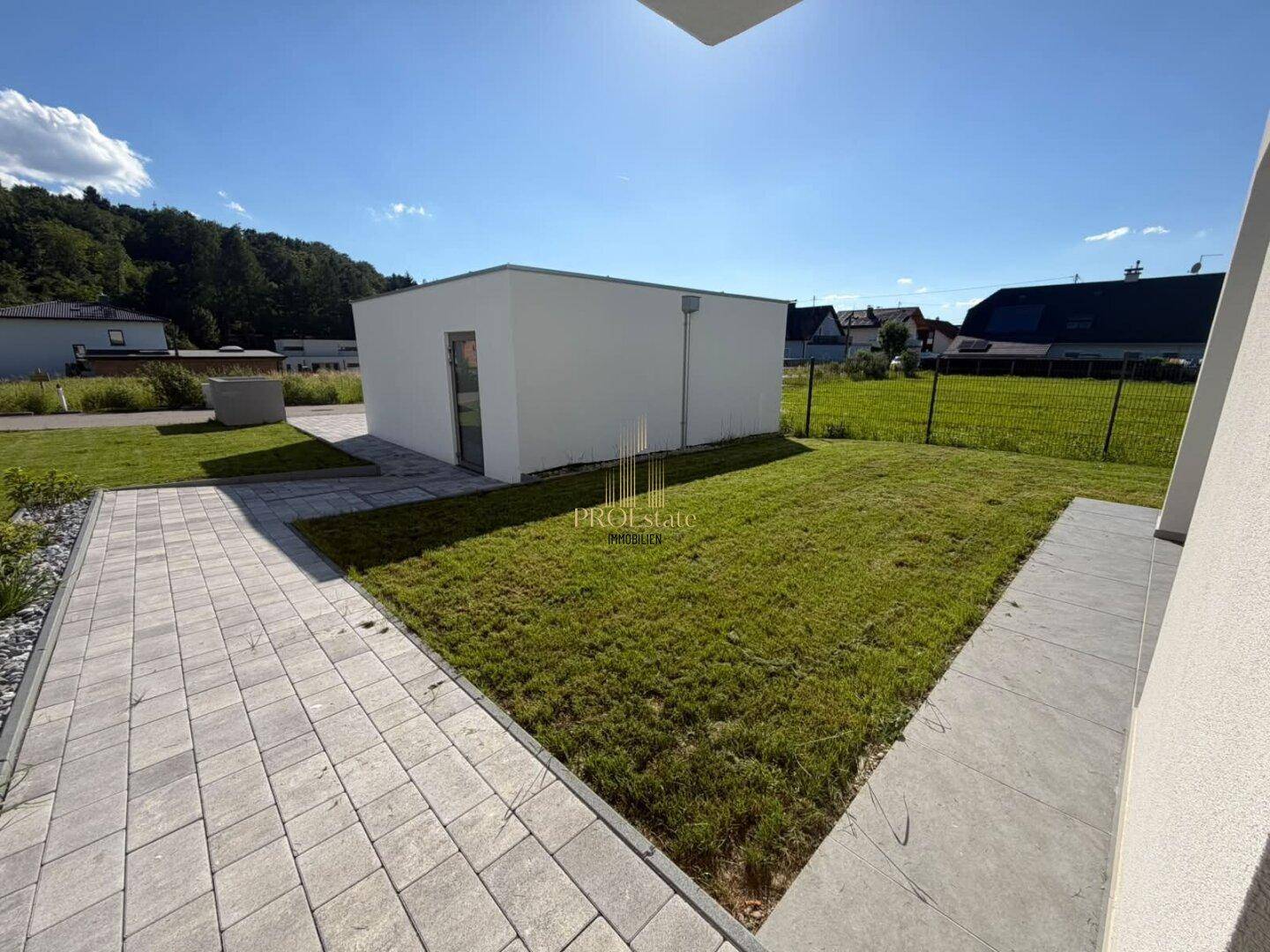 Großer Gartenbereich mit gepflasterter Terrasse, Rasenfläche und Blick auf die umliegende Landschaft.