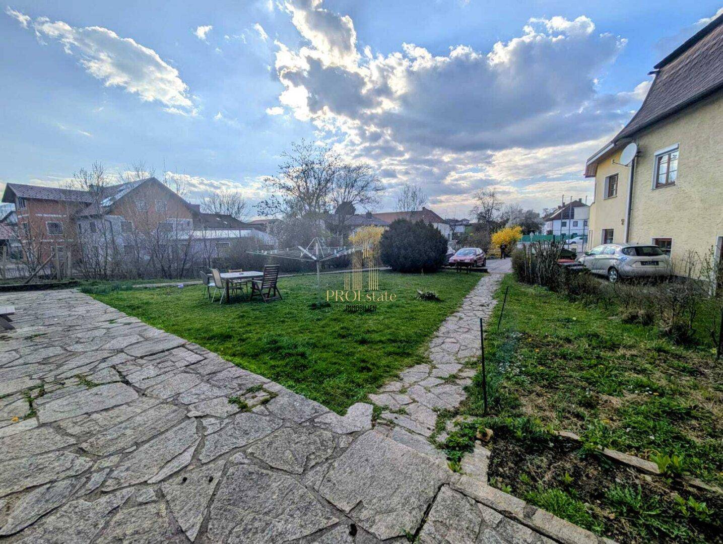 Großer Gartenbereich mit Rasenfläche, Steinplattenweg und Sitzgelegenheiten im Freien.