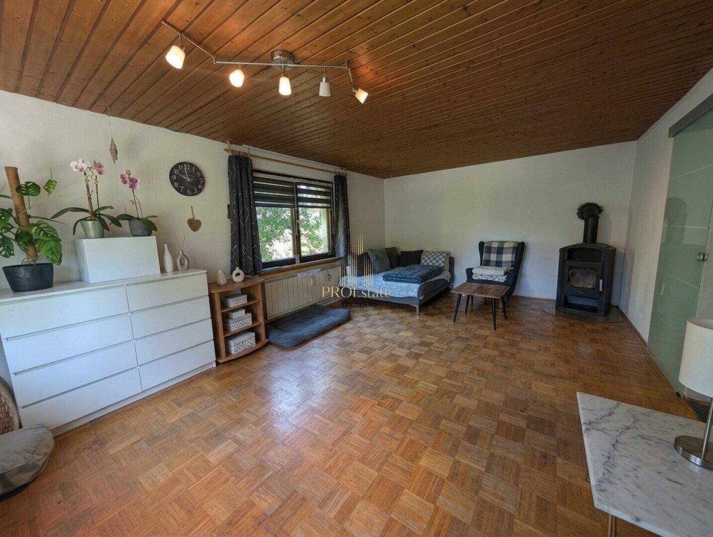 Gemütliches Wohnzimmer mit Parkettboden, Holzdecke und einem traditionellen Holzofen.
