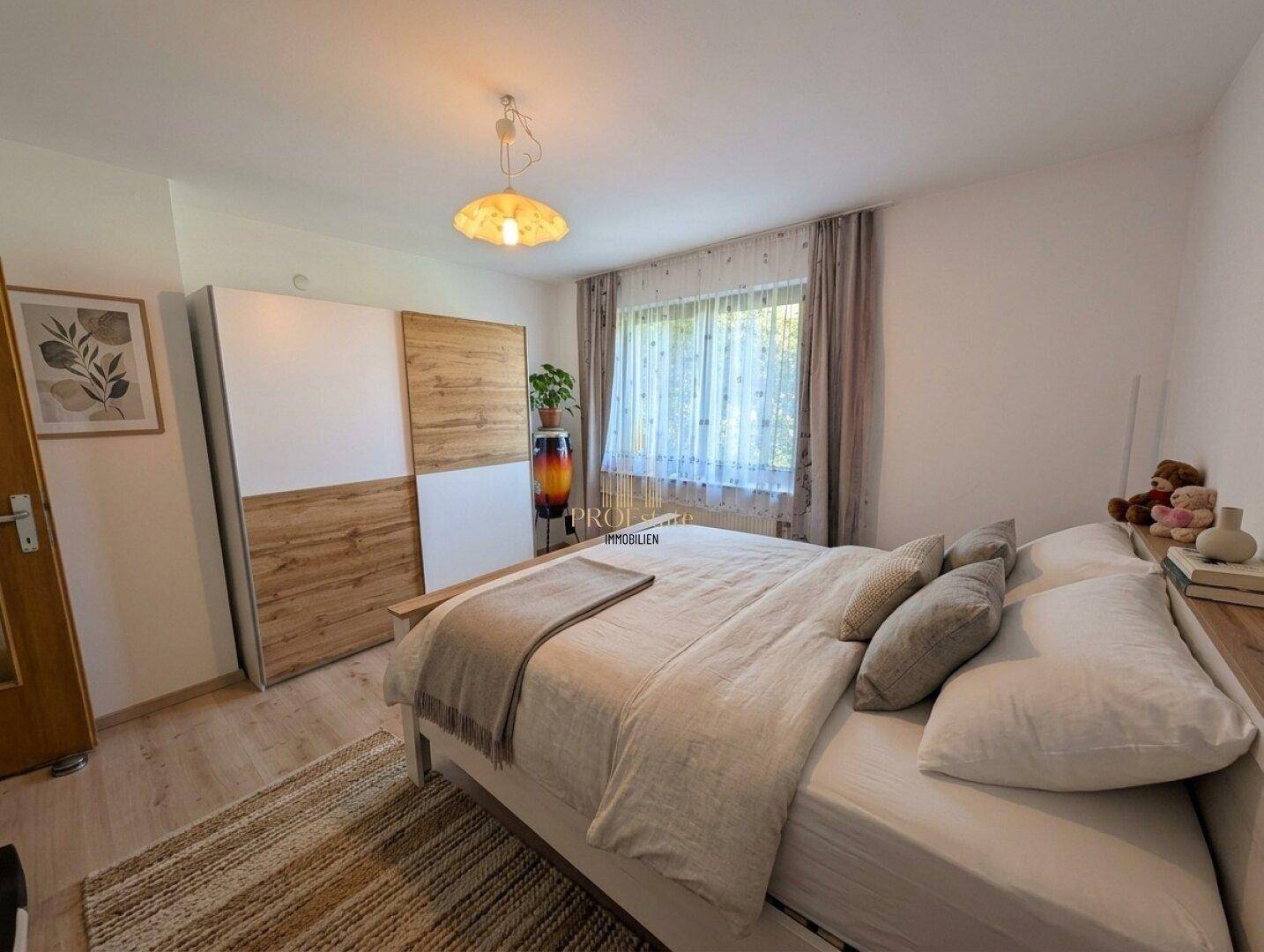 Schlafzimmer mit Doppelbett, Holzschrank und Blick ins Grüne durch das Fenster.