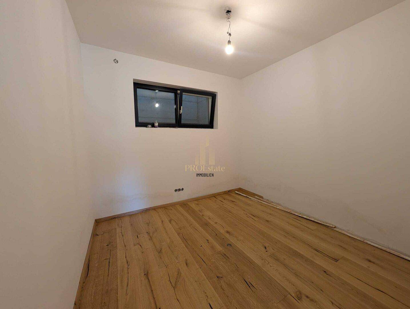 Helles Schlafzimmer mit Holzboden und einem Fenster, bereit zur individuellen Gestaltung.