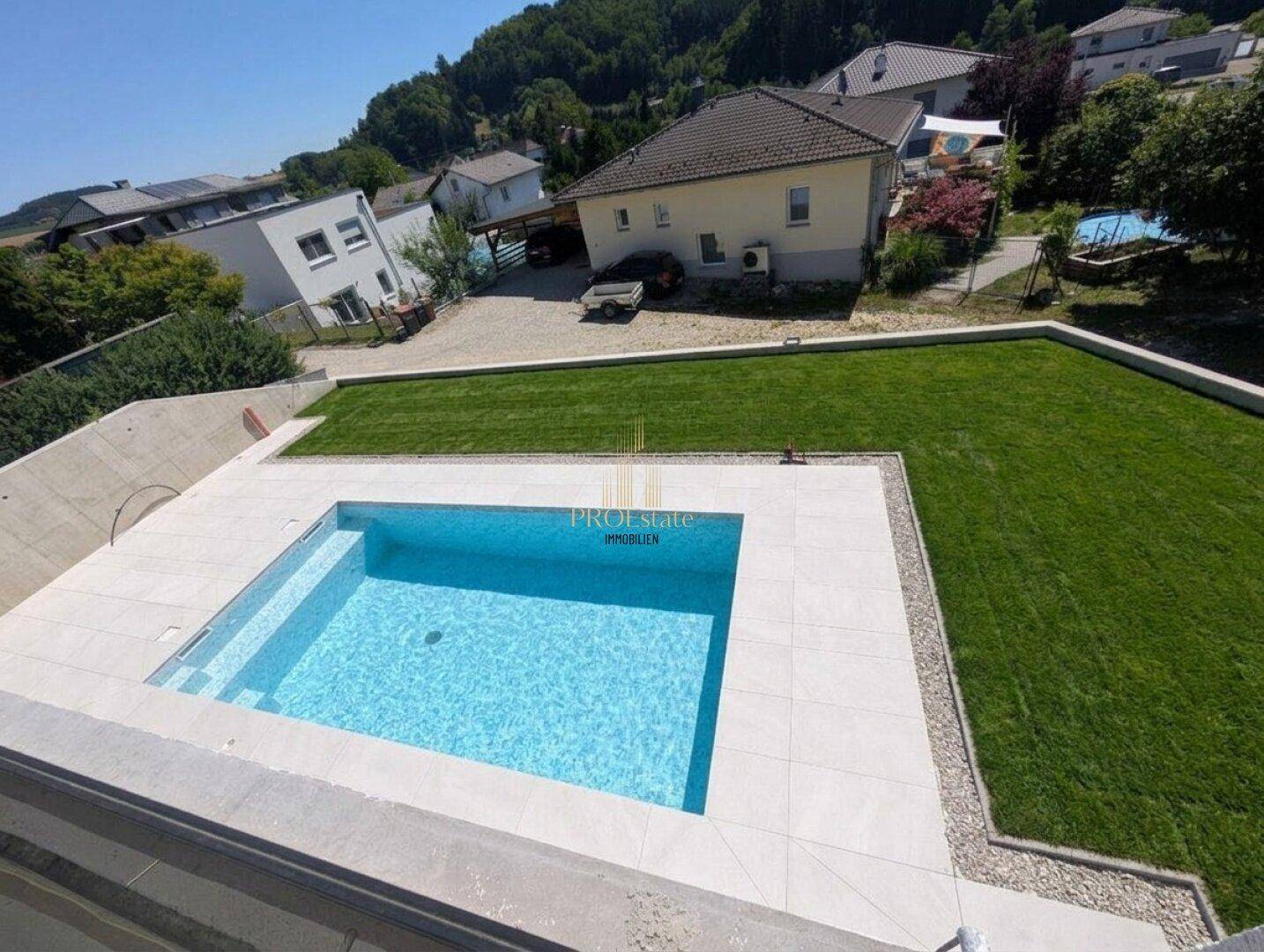 Außenbereich mit modernem Swimmingpool und weitläufiger Rasenfläche, umgeben von Natur.