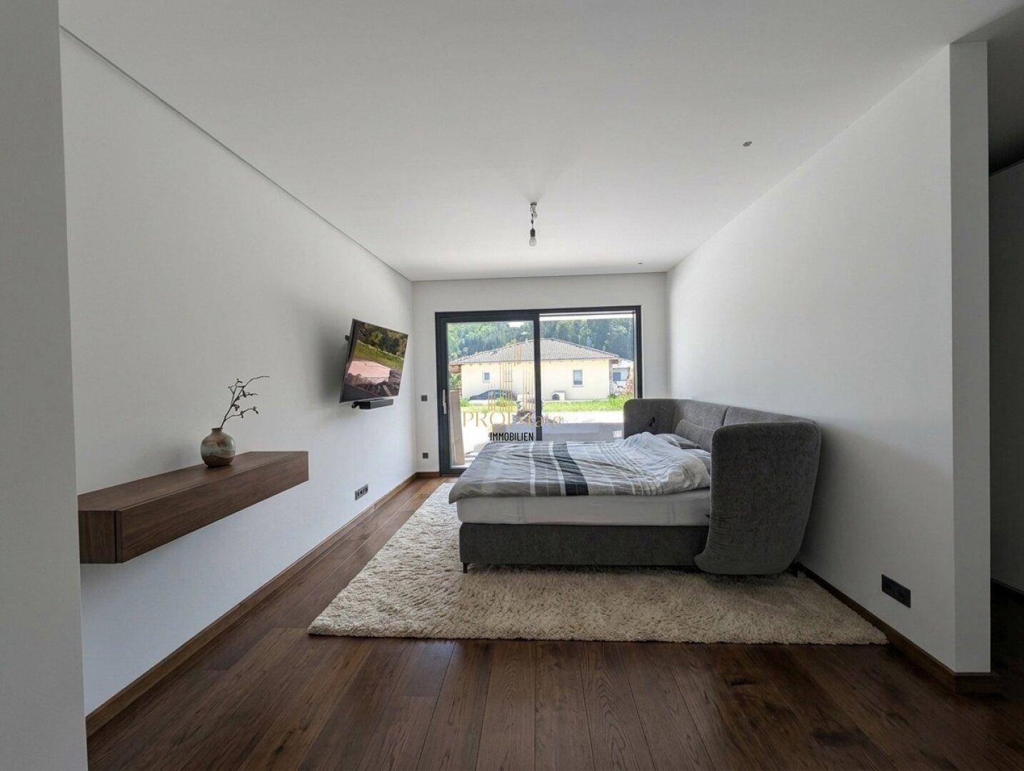 Modernes Schlafzimmer mit Holzboden, Wandfernseher und großem Fenster.