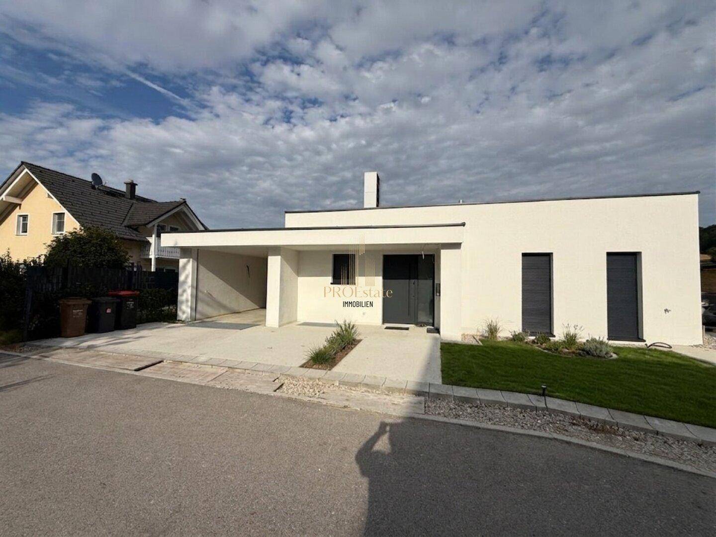 Moderne Hausfassade mit Carport und gepflegtem Vorgarten unter blauem Himmel.