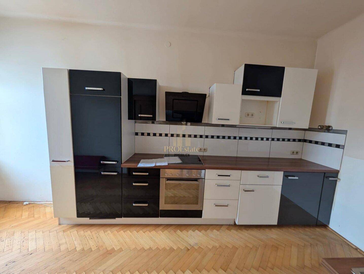 Moderne Küche mit schwarzen und weißen Schränken, integriertem Backofen und Kochfeld auf Parkettboden.