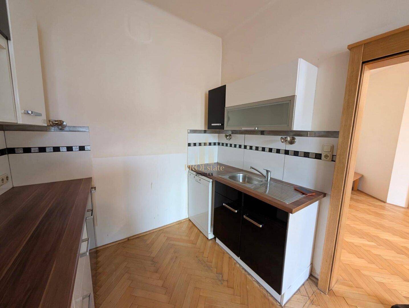 Kleine Küchenzeile mit Spülbecken, Holz-Arbeitsplatte und weißen Fliesen als Spritzschutz auf Parkettboden.