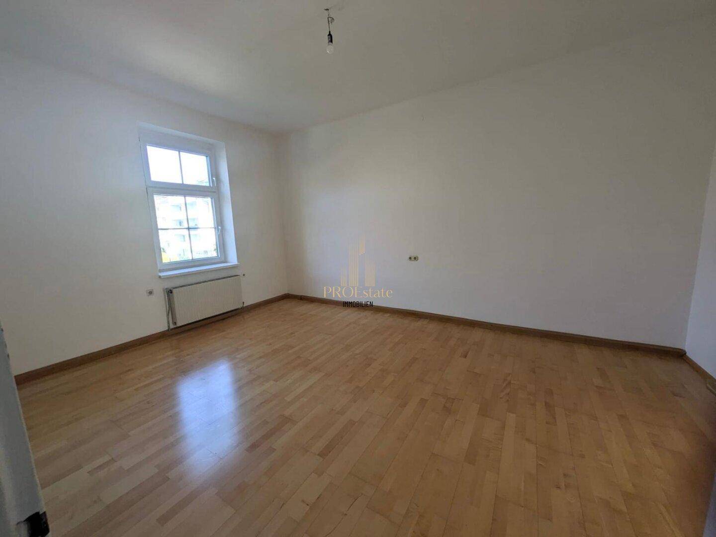 Leeres Zimmer mit hellem Holzboden, weiß gestrichenen Wänden und einem Fenster für natürliches Licht.