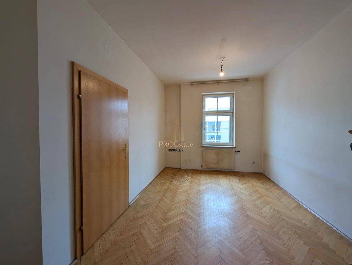 Helles Zimmer mit Fischgrätparkett, weiß gestrichenen Wänden und einem Fenster für Tageslicht.