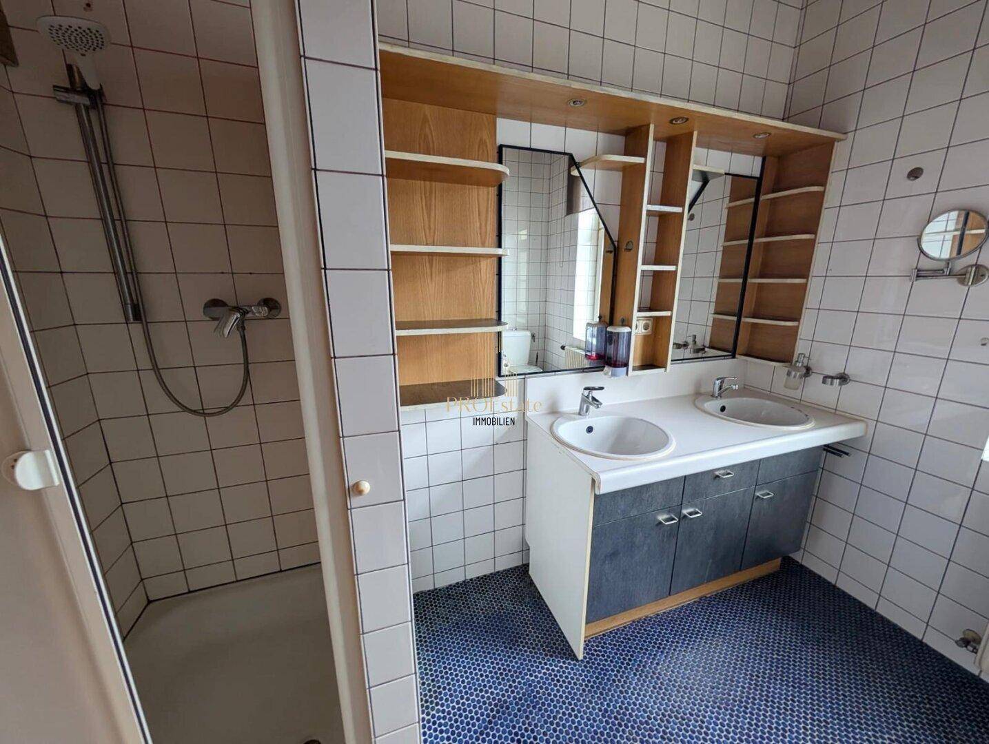 Badezimmer mit Dusche, Doppelwaschbecken und Spiegelschrank über blauen Mosaikfliesen am Boden.