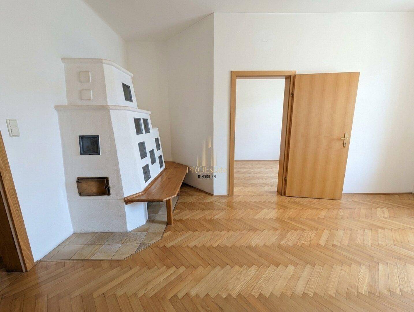 Helles Zimmer mit traditionellem Kachelofen, integrierter Sitzbank und klassischem Fischgrätparkett.
