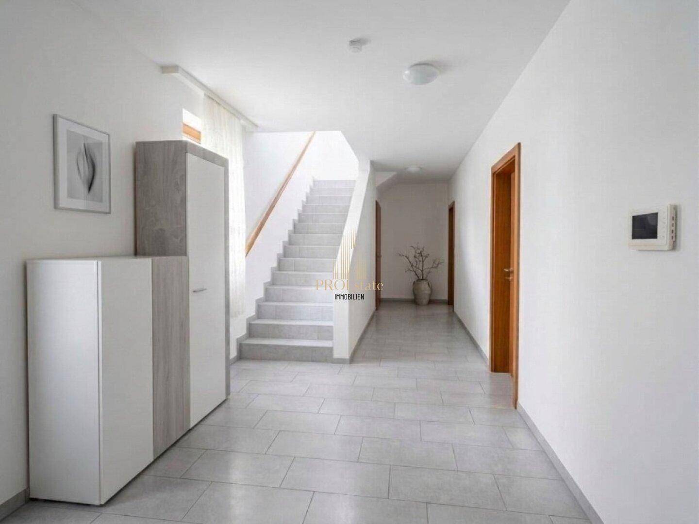 Heller Flur mit Fliesenboden, Treppe und Garderobenschrank.