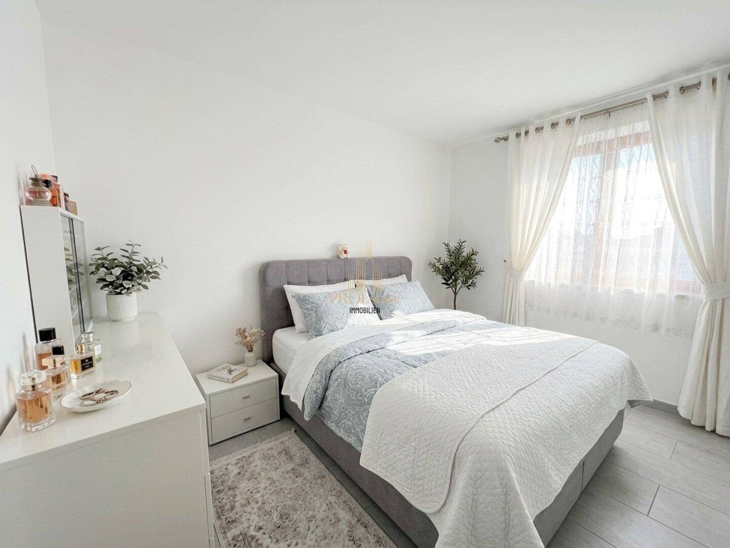 Helles Schlafzimmer mit Doppelbett, Kommode und Fenster.