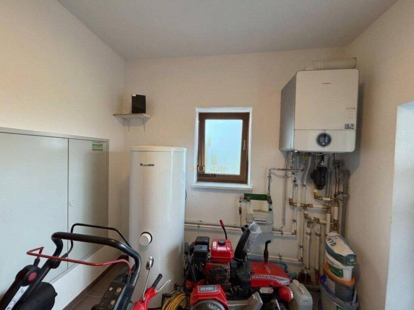 Technikraum mit Heizungsanlage, Warmwasserspeicher und Fenster.