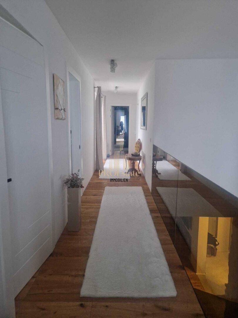 Langer, heller Flur mit Holzboden und Glasgeländer, das den Blick in die untere Etage freigibt.