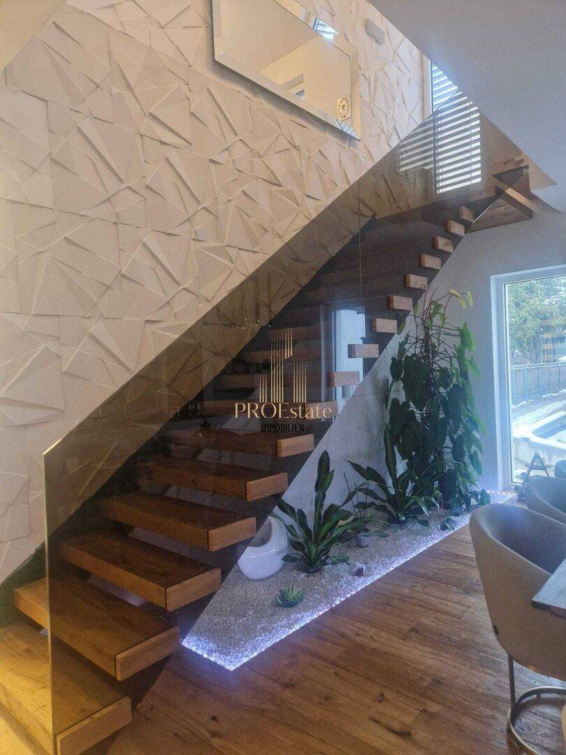 Elegante moderne Treppe mit Glasgeländer und dekorativer Pflanzeninsel unterhalb.