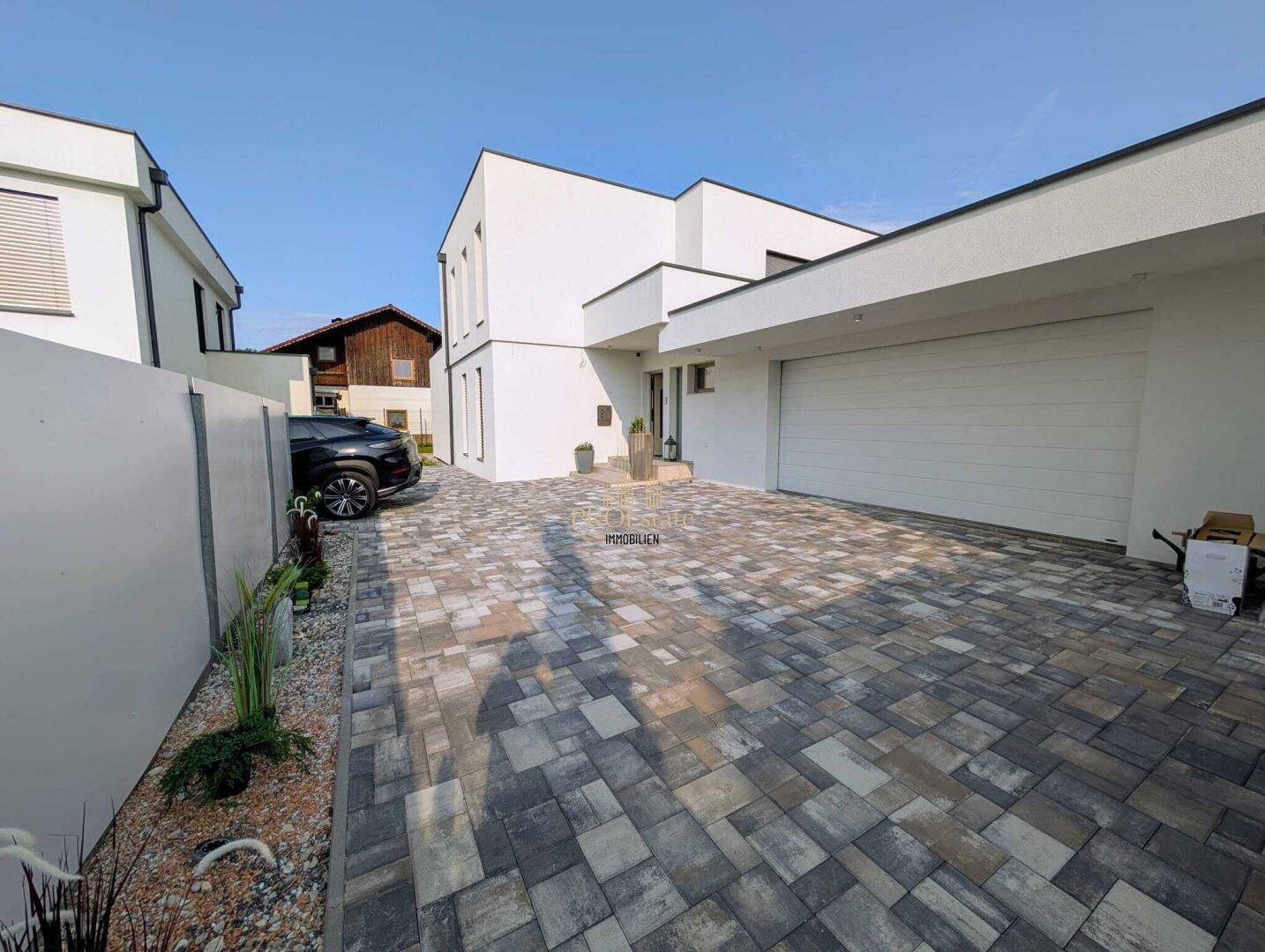 Moderne Hausfassade mit großer gepflasterter Einfahrt und integrierter Doppelgarage.