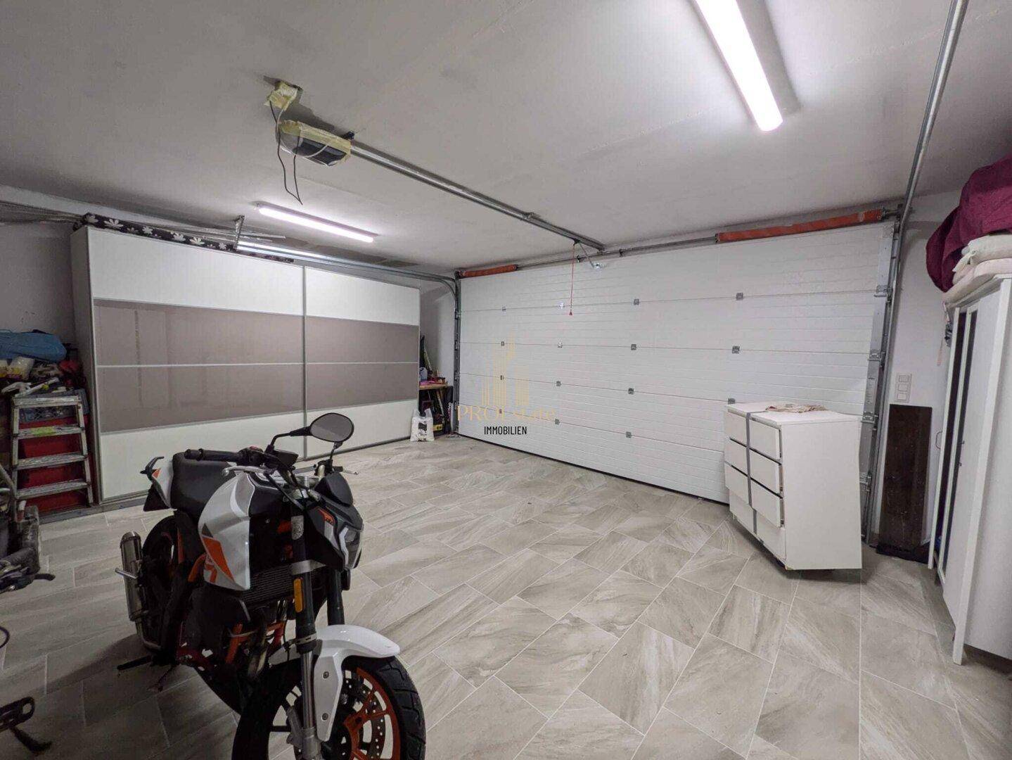 Geräumige Garage mit Fliesenboden, Stauraum und Platz für Fahrzeuge und Motorräder.