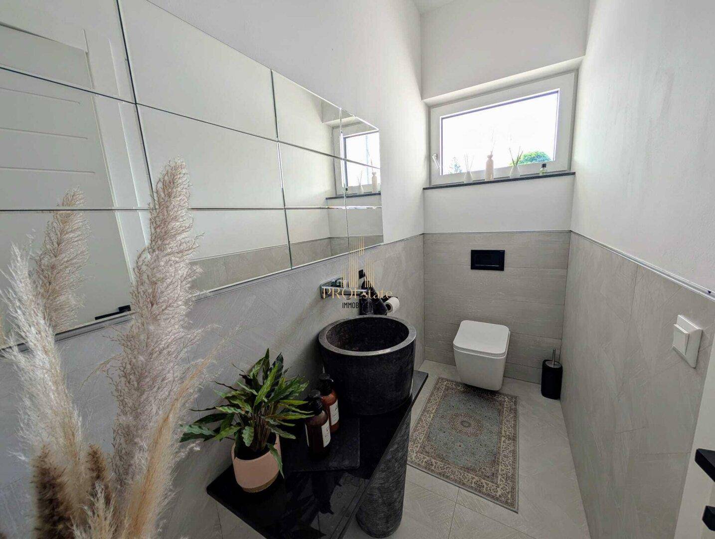 Modernes Gäste-WC mit dunklem Steinwaschbecken, wandhängendem WC und Fenster.