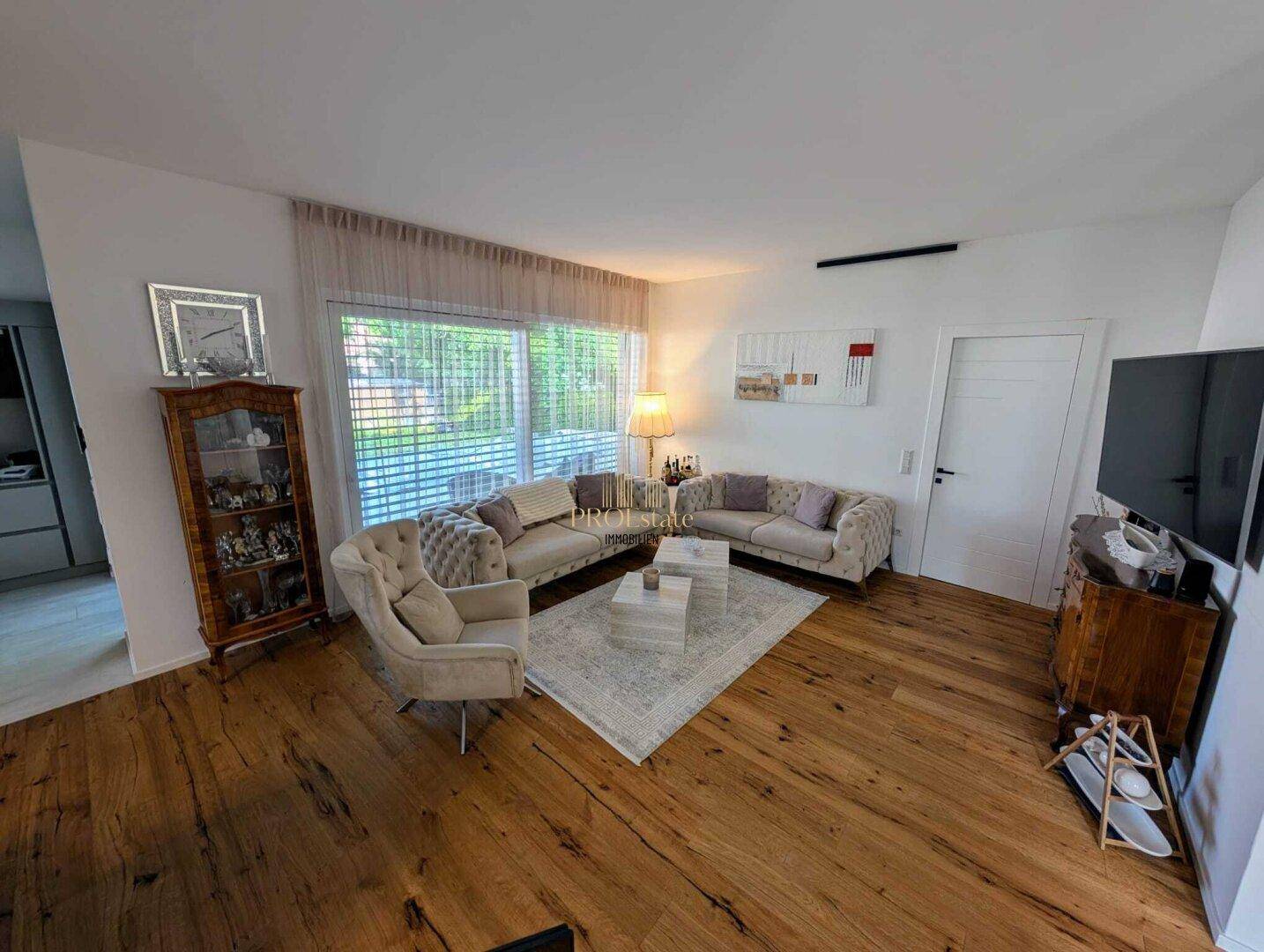 Gemütliches Wohnzimmer mit bequemen Sofas, Holzboden und großen Fenstern für viel Tageslicht.