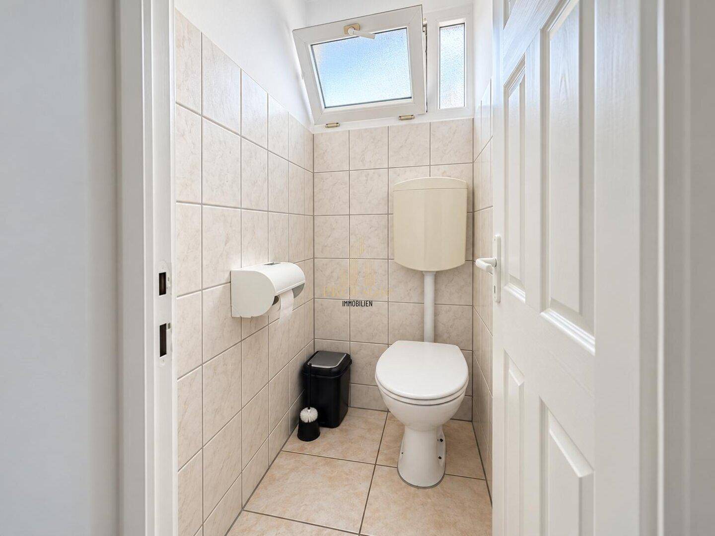 Kleiner Toilettenraum mit WC, gefliesten Wänden und einem Fenster für natürliche Belüftung.