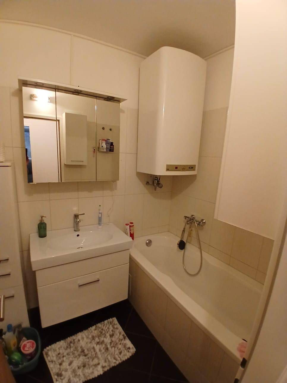 Badezimmer mit Badewanne, Waschbecken, Spiegelschrank und einem Warmwasserboiler.