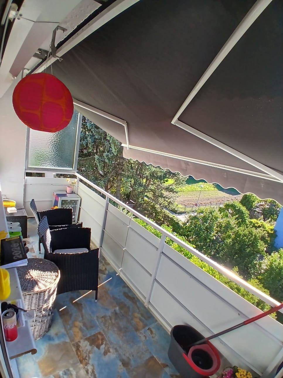 Möblierter Balkon mit Markise, Fliesenboden und Blick ins Grüne und auf die Landschaft.