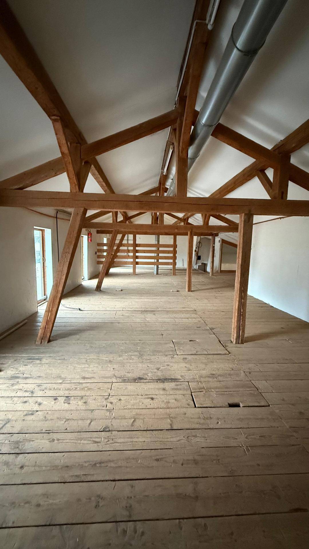 Heller Dachboden mit freiliegenden Holzsparren und robustem Holzboden, bietet eine offene und vielseitige Fläche.