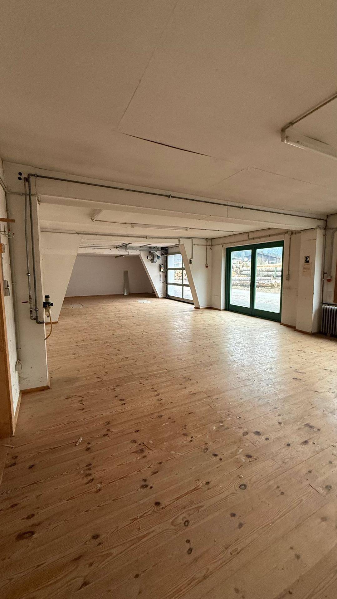Weiterer Blick in den geräumigen Gewerberaum mit Holzboden und großen Fenstern, die viel Tageslicht hereinlassen.