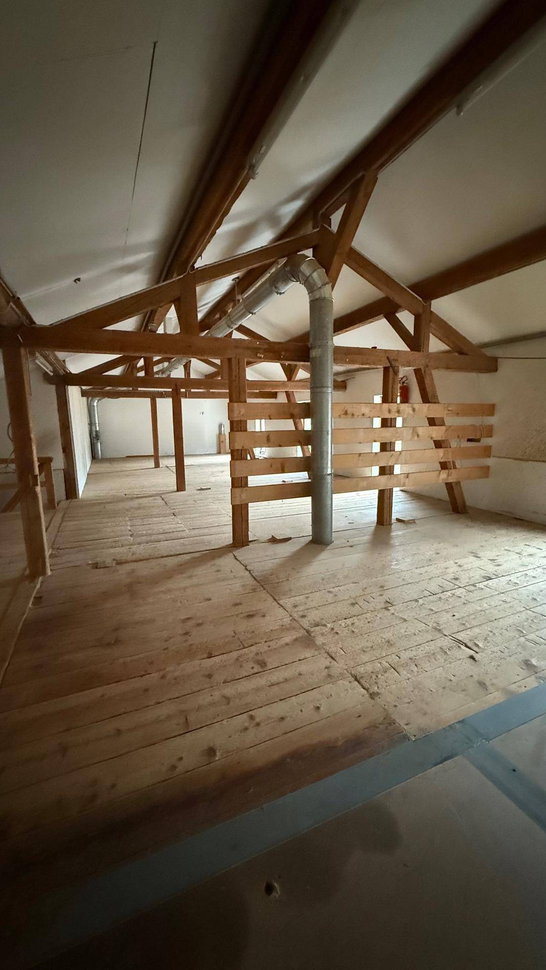 Offener Dachbodenbereich mit markanten Holzbalken und einem zentralen Lüftungsrohr, bereit für die Gestaltung.