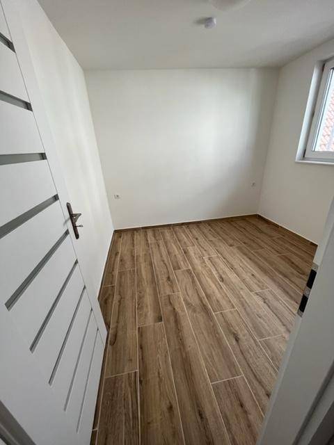 Schlafzimmer mit Holzoptik-Fliesenboden und einem Fenster, das für ausreichend Tageslicht sorgt.