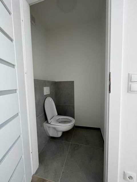 Modernes Gäste-WC mit Wand-WC und grauen Fliesen an Wänden und Boden, minimalistisch und funktional.