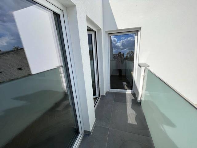 Schmaler Balkon mit Fliesenboden und Glasgeländer, ideal für frische Luft und einen kleinen Sitzbereich.