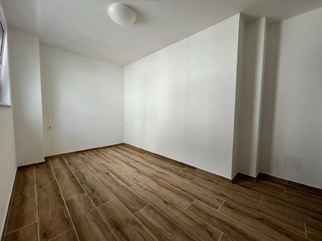 Geräumiges Schlafzimmer mit Holzoptik-Fliesenboden und weißen Wänden, bereit zur individuellen Gestaltung.