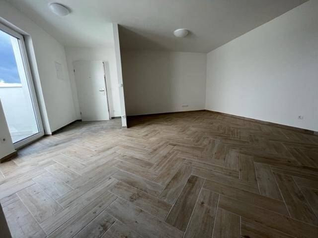 Heller Wohnbereich mit Fischgrätmuster-Fliesenboden und Zugang zu einem Balkon, bietet viel Tageslicht.