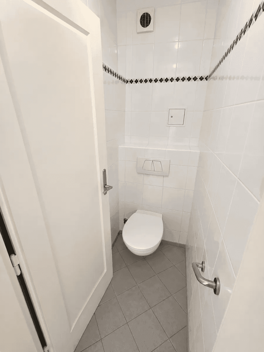 Kleines Gäste-WC mit wandhängender Toilette, weißen Fliesen und Haltegriff.