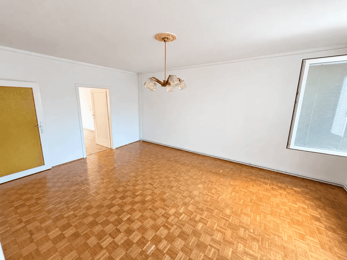 Geräumiges Wohnzimmer mit klassischem Parkettboden, weißen Wänden und gelber Tür.