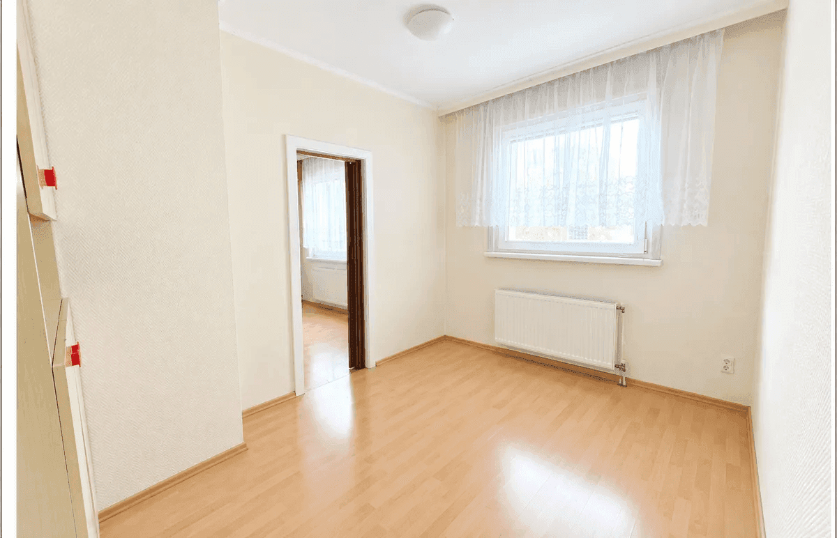 Helles Schlafzimmer mit hellem Holzboden, Fenster und Zugang zu einem weiteren Raum.