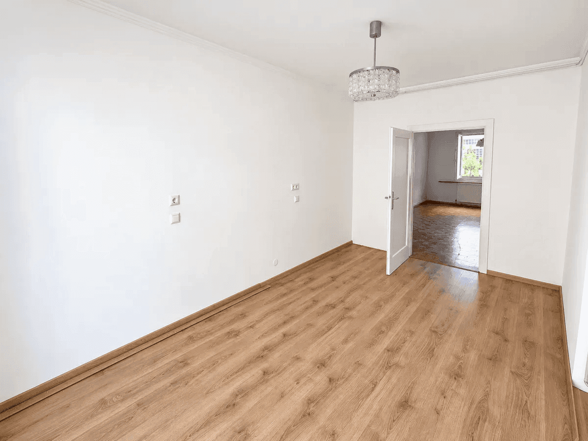 Heller, leerer Raum mit modernem Laminatboden und weiß gestrichenen Wänden.