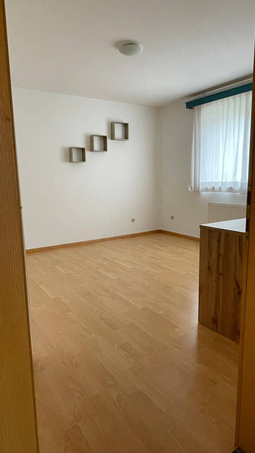 Helles Schlafzimmer mit Holzboden und einem Fenster, das viel Tageslicht hereinlässt.