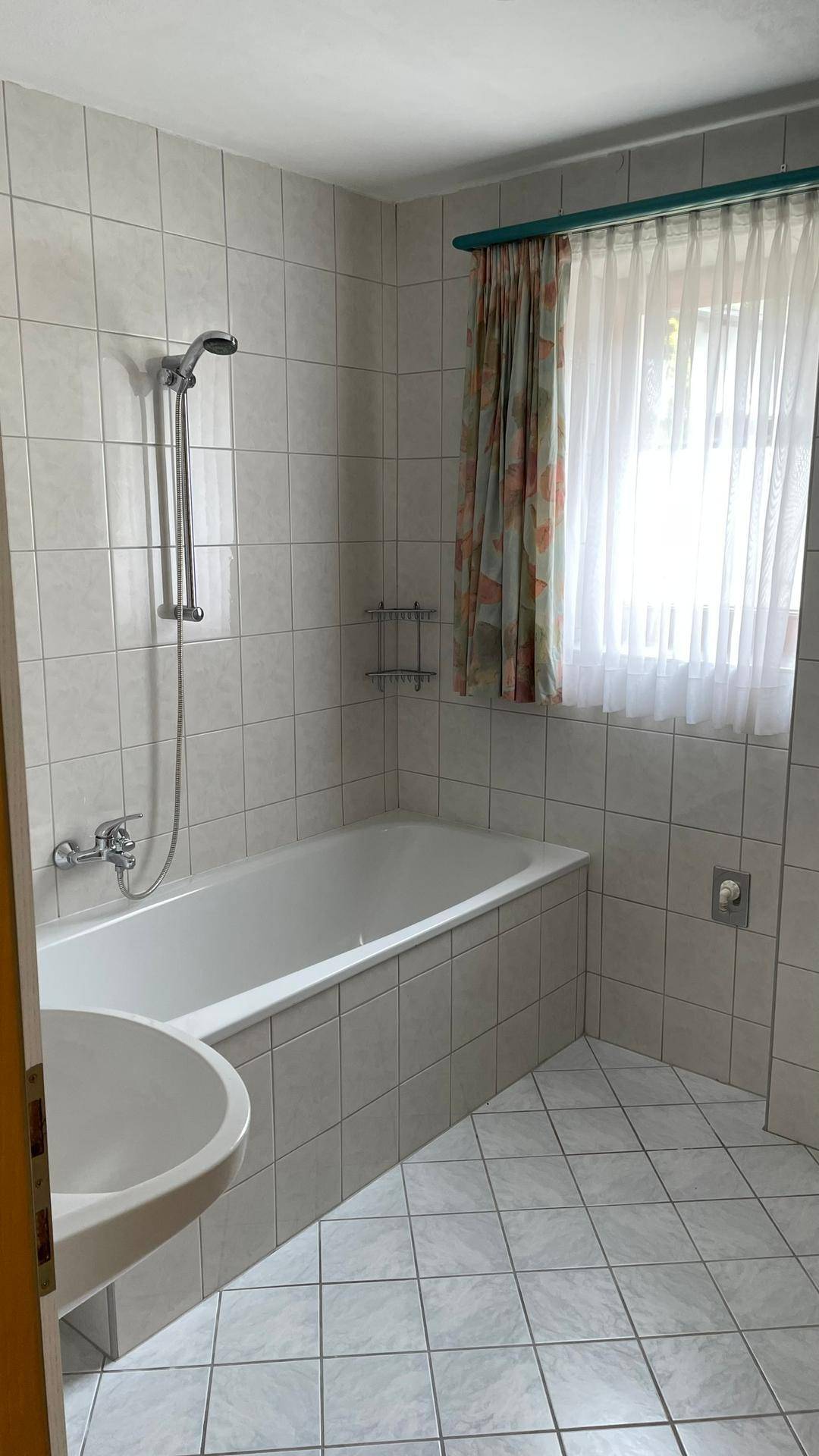 Gefliestes Badezimmer mit Badewanne, Duschfunktion, Waschbecken und einem Fenster für Tageslicht.