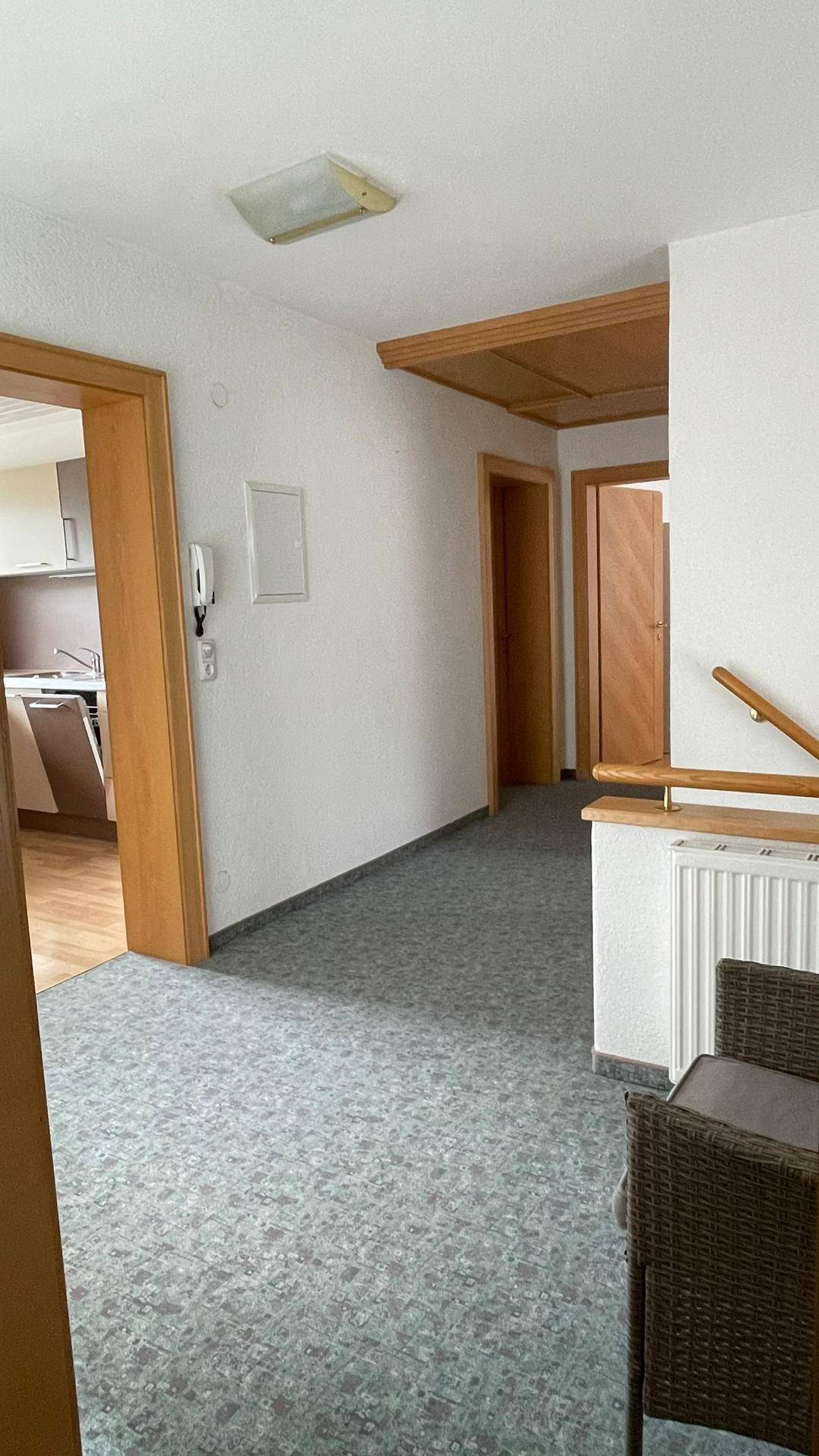 Heller Flur mit Teppichboden, Holzvertäfelung an der Decke und Zugang zu weiteren Räumen.