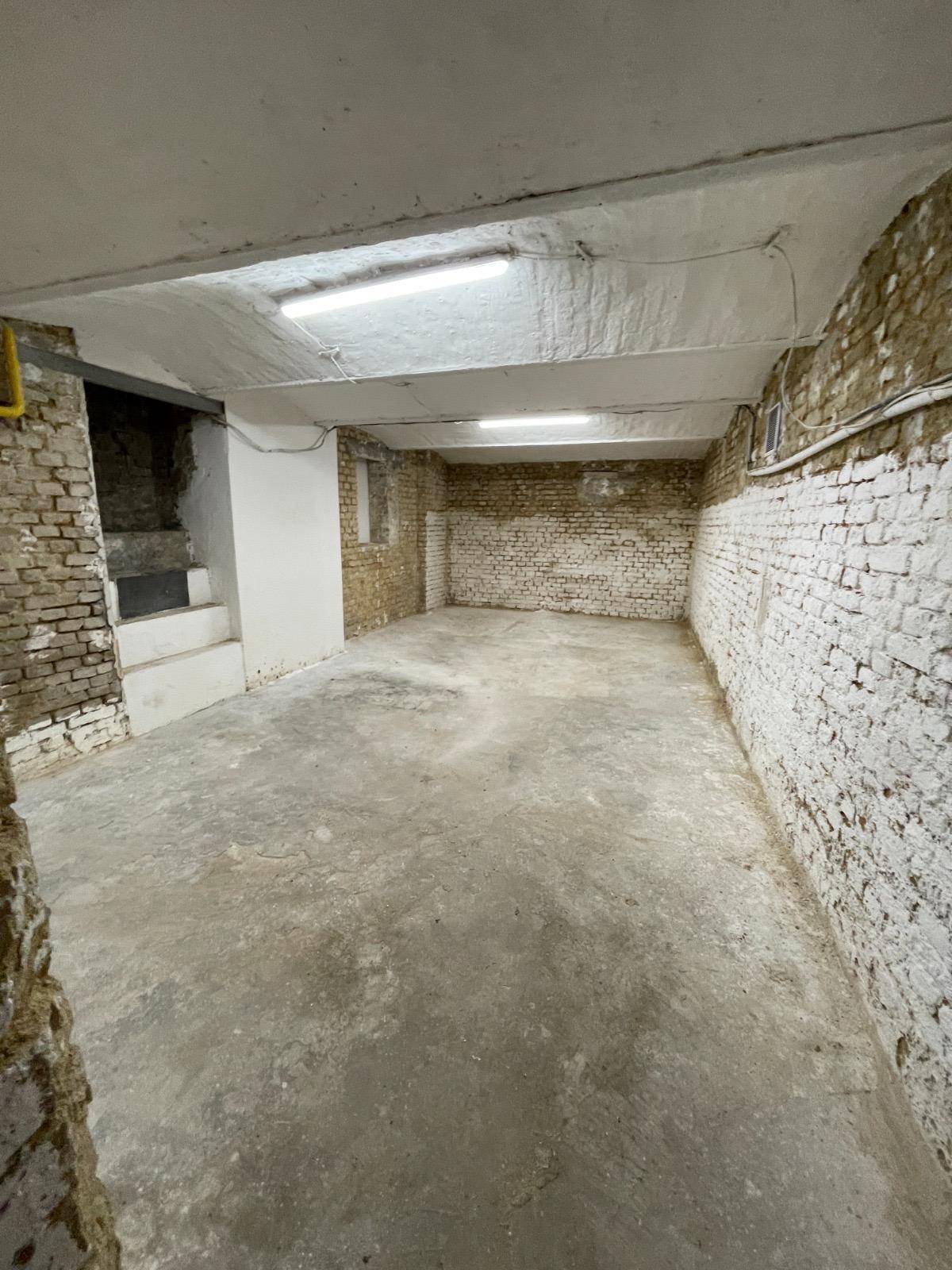 Großer, leerer Kellerraum mit teilweise weiß gestrichenen Ziegelwänden und Betonboden.
