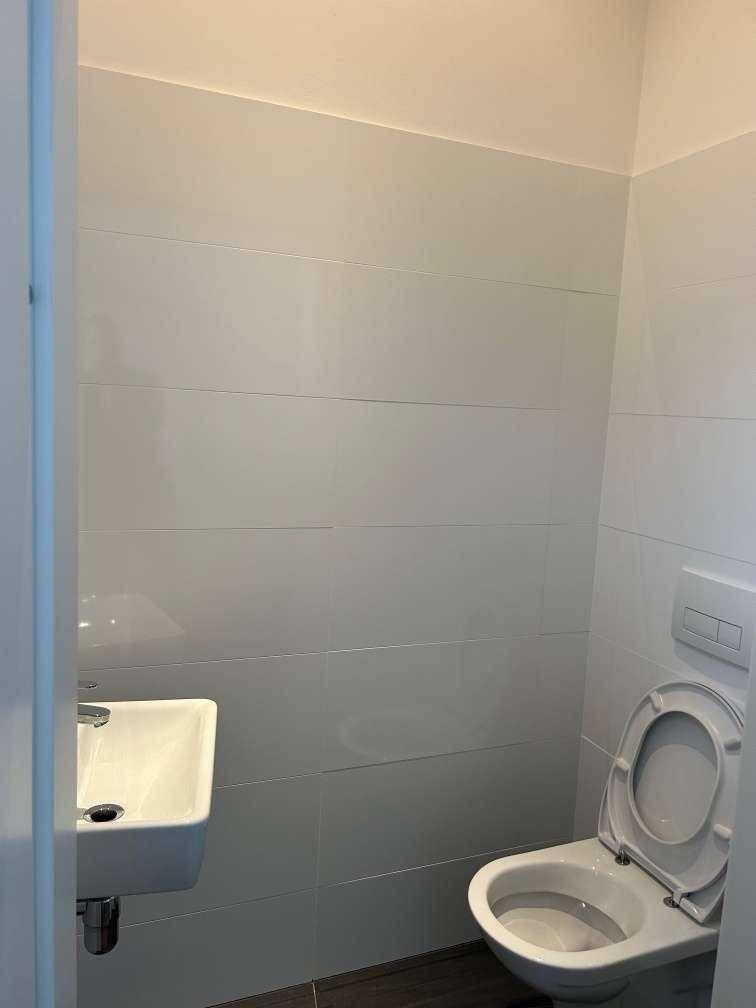 Modern gefliestes Gäste-WC mit wandhängender Toilette und kleinem Waschbecken in hellem Design.