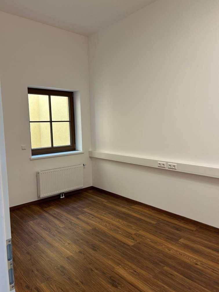 Kleiner, heller Raum mit einem Fenster, Holzboden und Heizkörper, geeignet als Einzelbüro oder Abstellraum.
